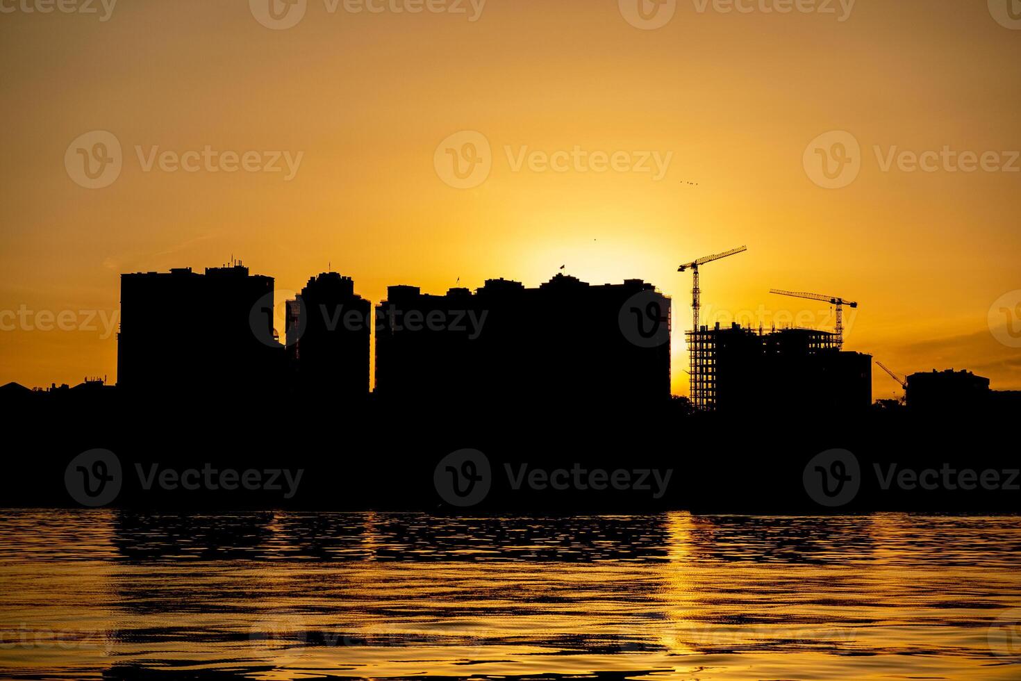 City skyline silhouette during sunset with cranes and buildings reflected in water photo
