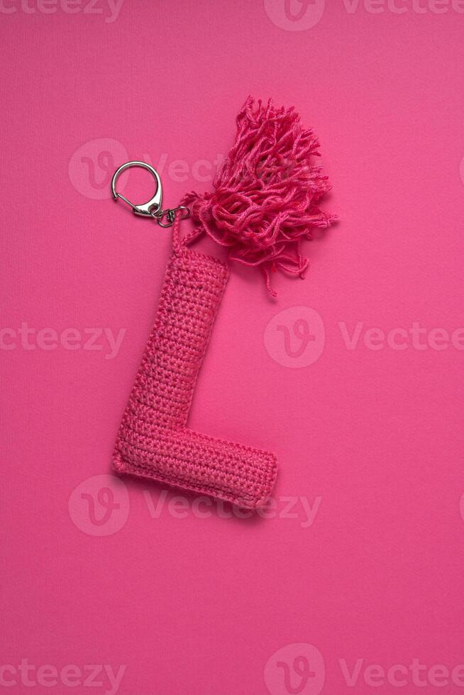 A pink crocheted keychain in the shape of the letter 'L' with a tassel, set against a matching pink background. photo