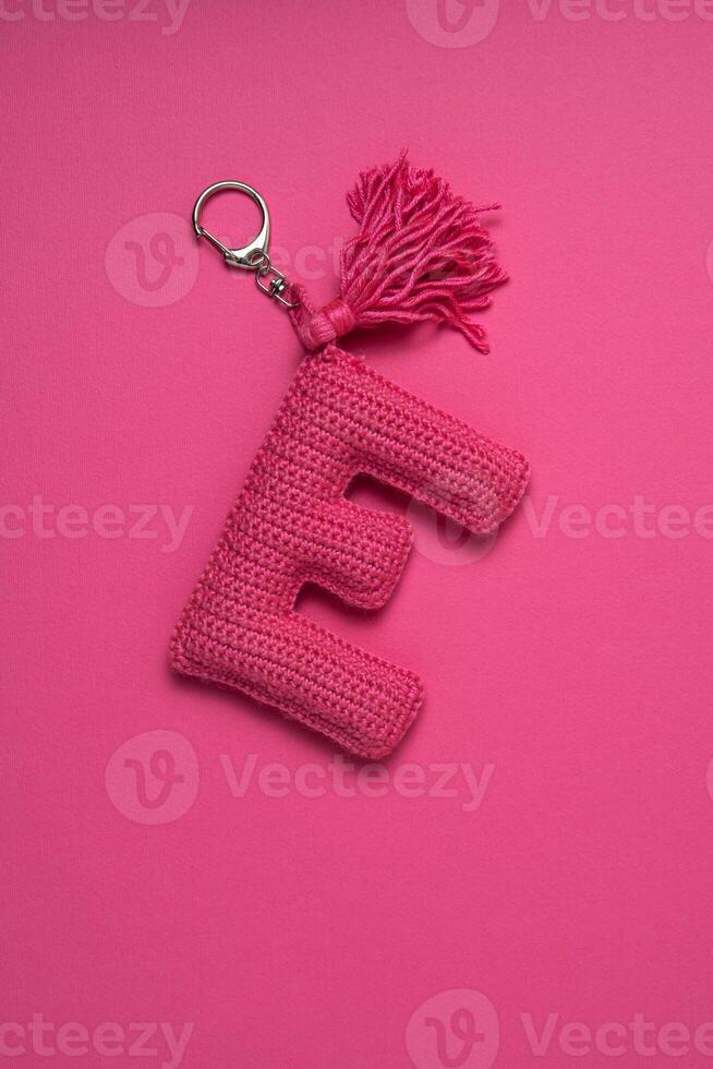 A pink crocheted keychain in the shape of the letter 'E' with a tassel, set against a matching pink background. photo