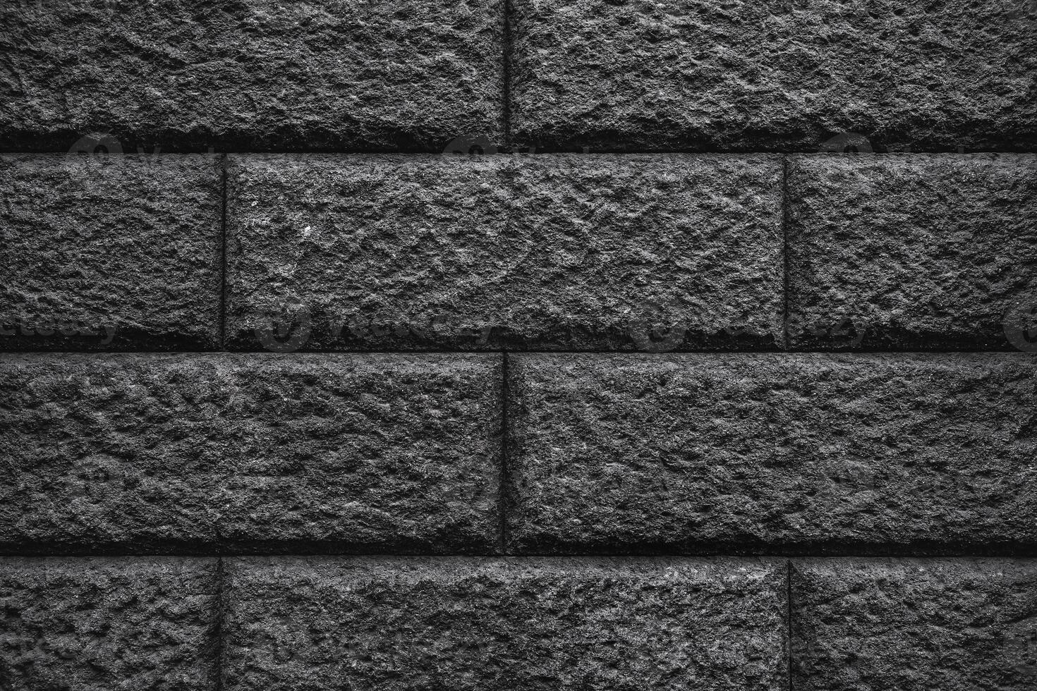 A textured wall of dark gray bricks, with a rough and uneven surface. The bricks are arranged in a traditional pattern. photo