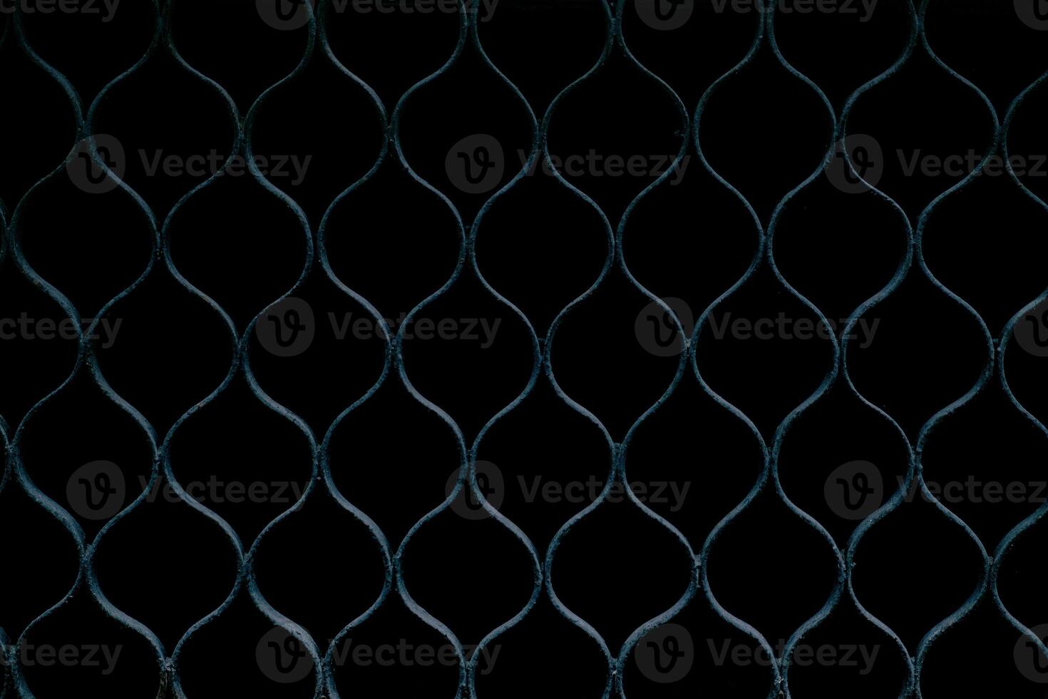 A close-up of a metal fence with a repeating diamond pattern, dark background. photo