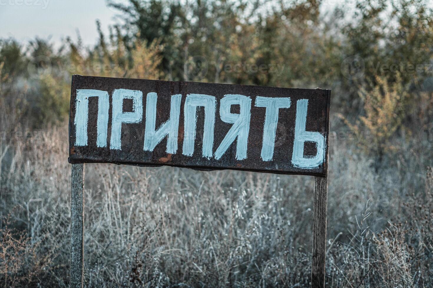 A weathered sign with the word in Cyrillic script, standing in an overgrown, abandoned area. photo