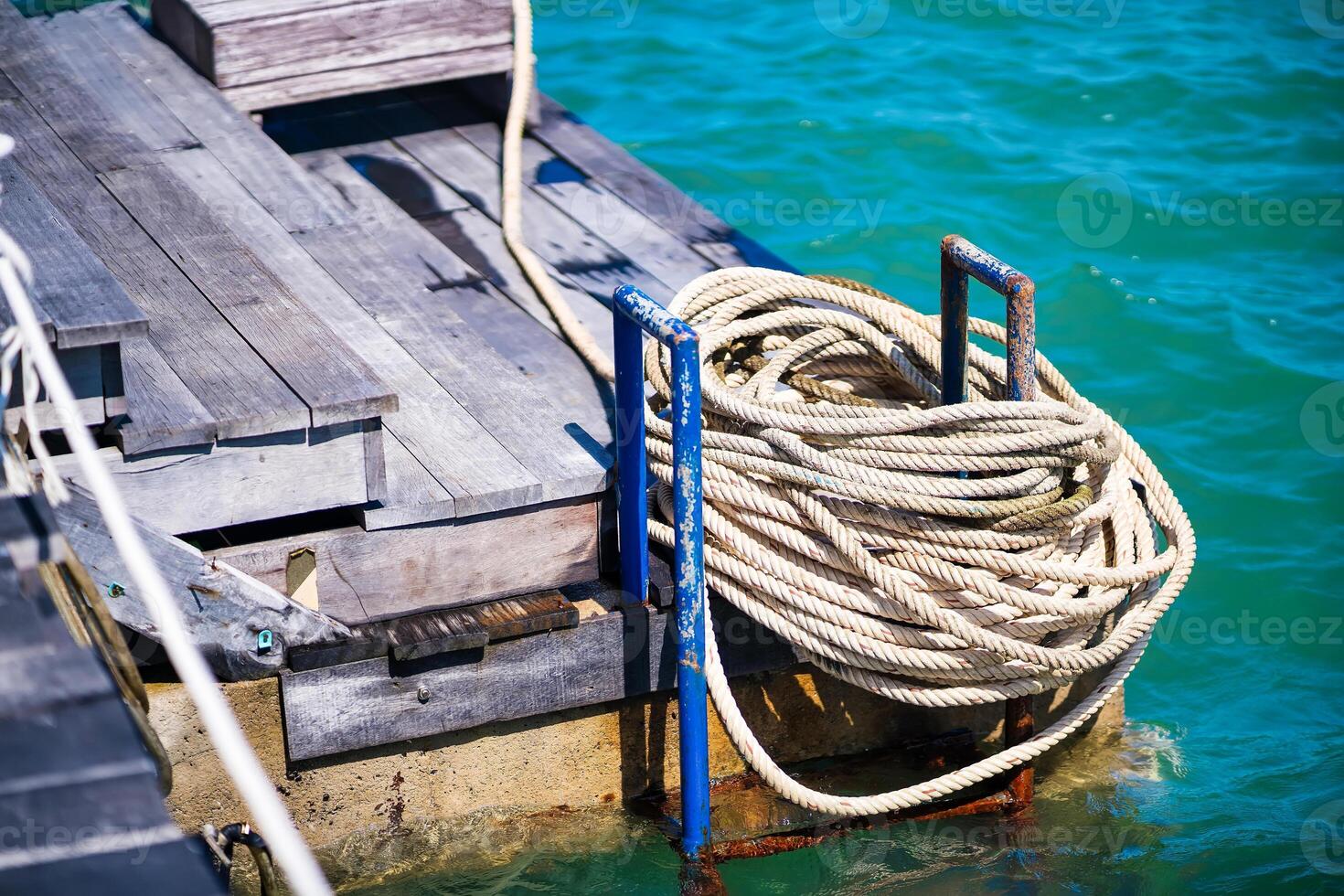 An inviting view of a rustic wooden dock with a neatly coiled rope, set against the stunning backdrop of a turquoise sea, perfect for any nautical-themed design. photo