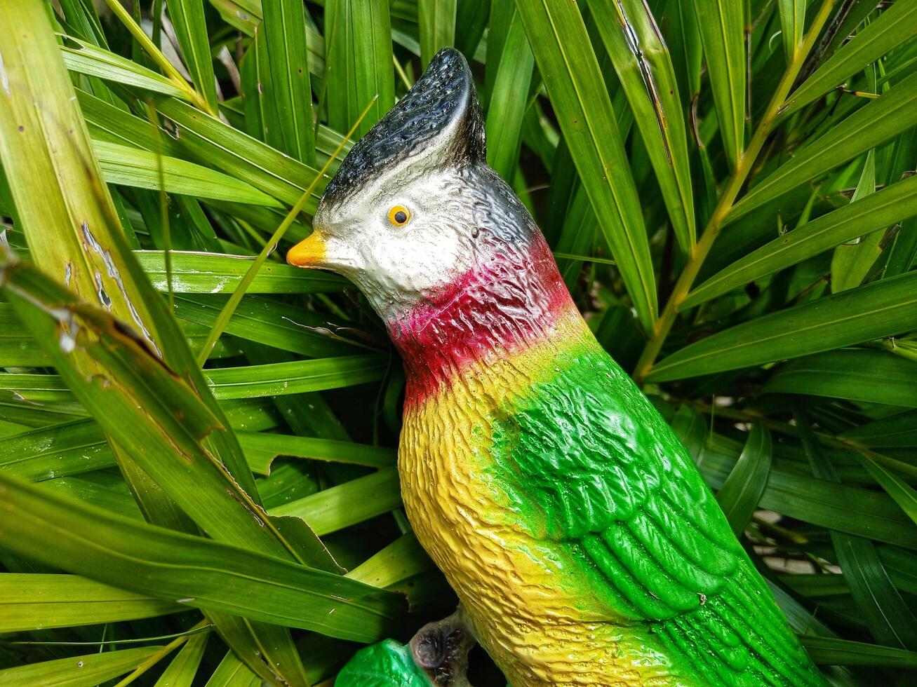 statue of a parrot animal character on a twig on a leaf background photo