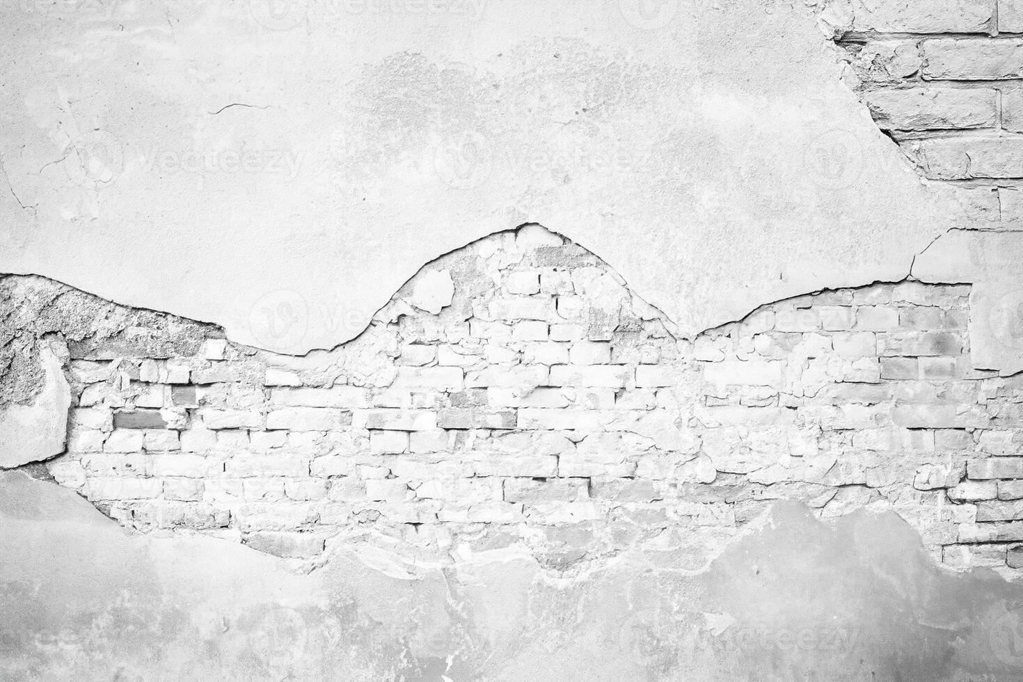 A cracked plaster wall revealing an underlying brick surface, suitable as a background texture for design projects. photo