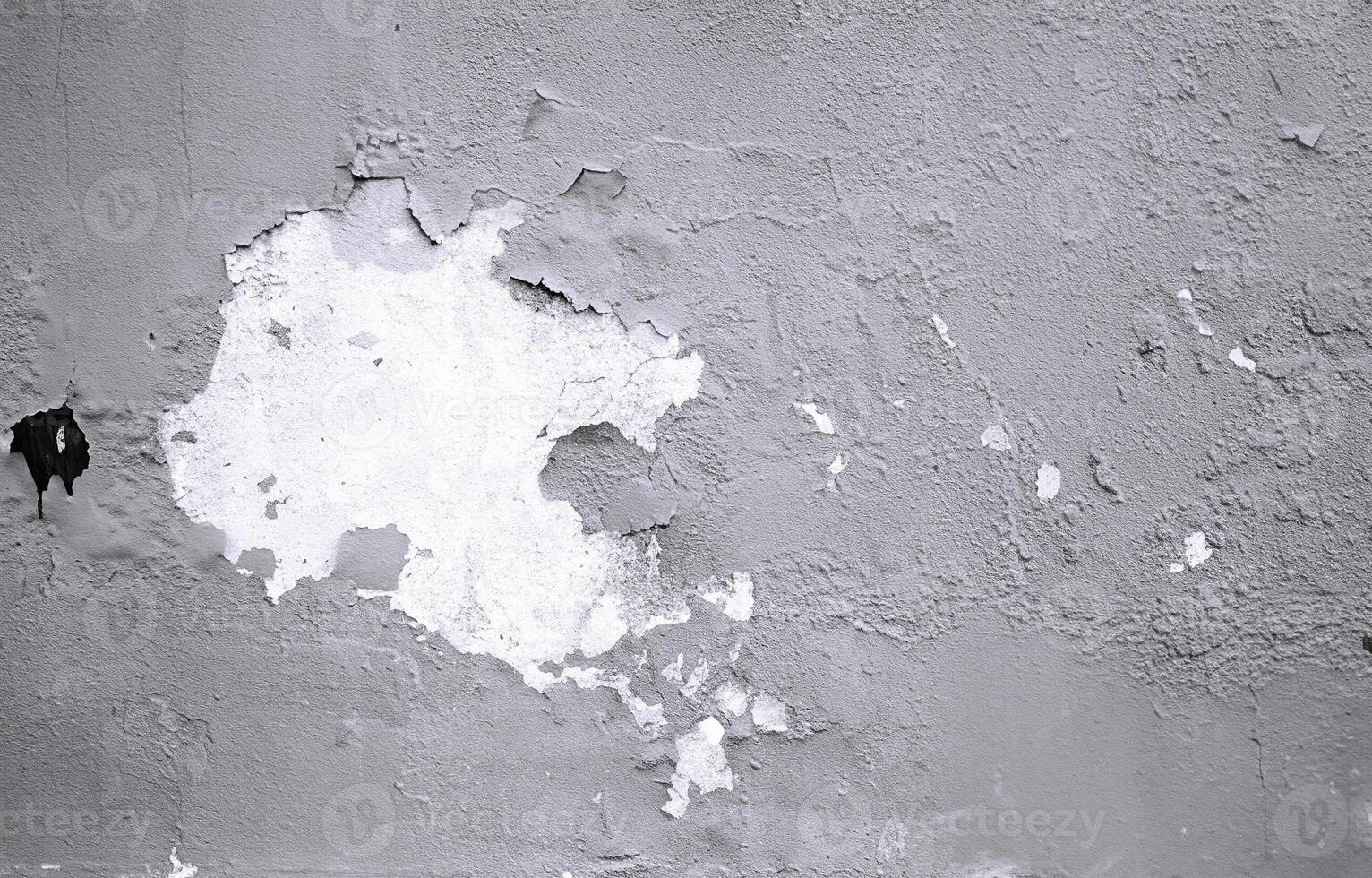 Close-up of a weathered wall showing peeling paint, cracks, and rough texture in a monochromatic tone. photo