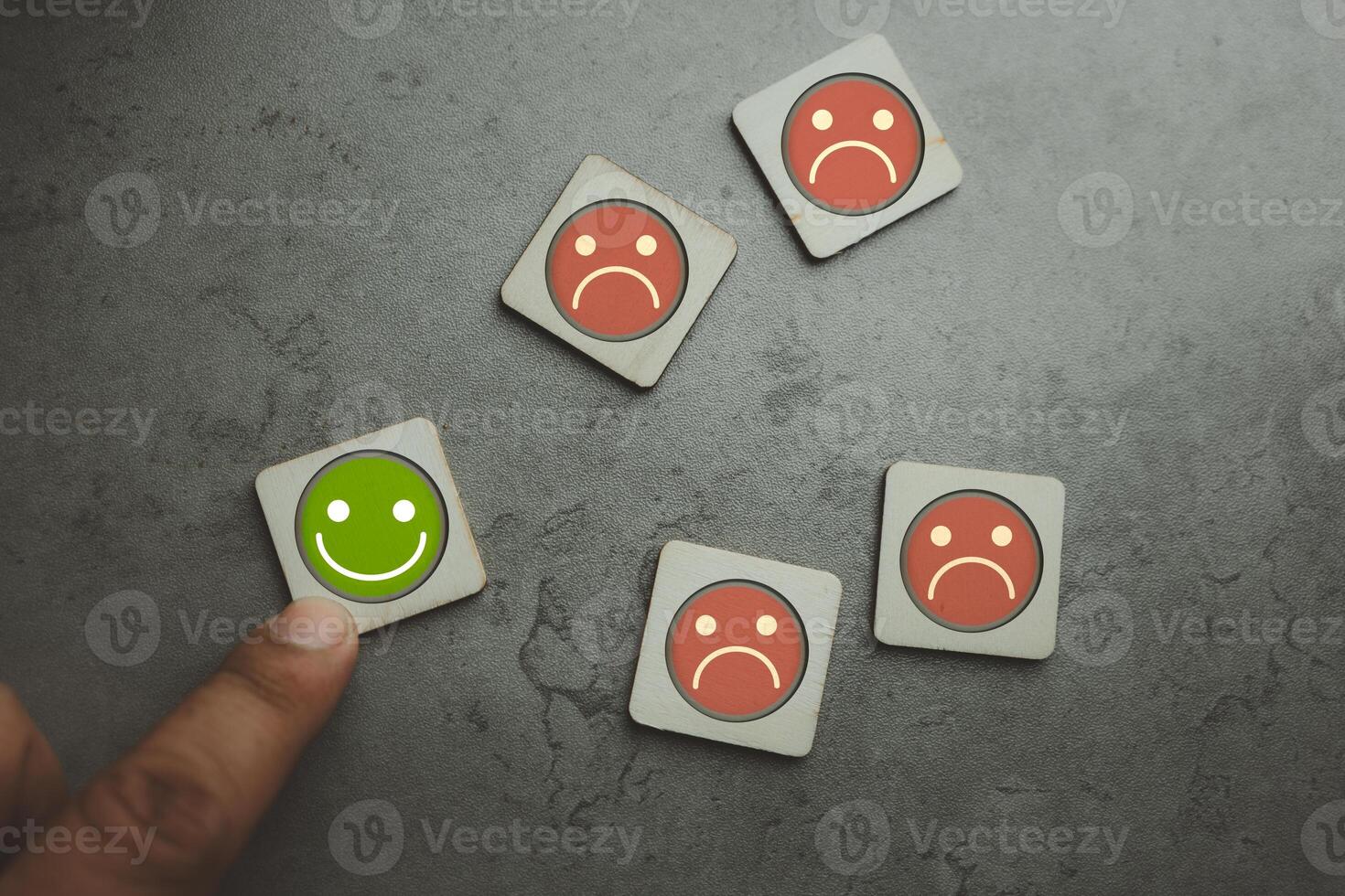 Hand choose happy face icon on wooden cube from the others on not happy on desk photo
