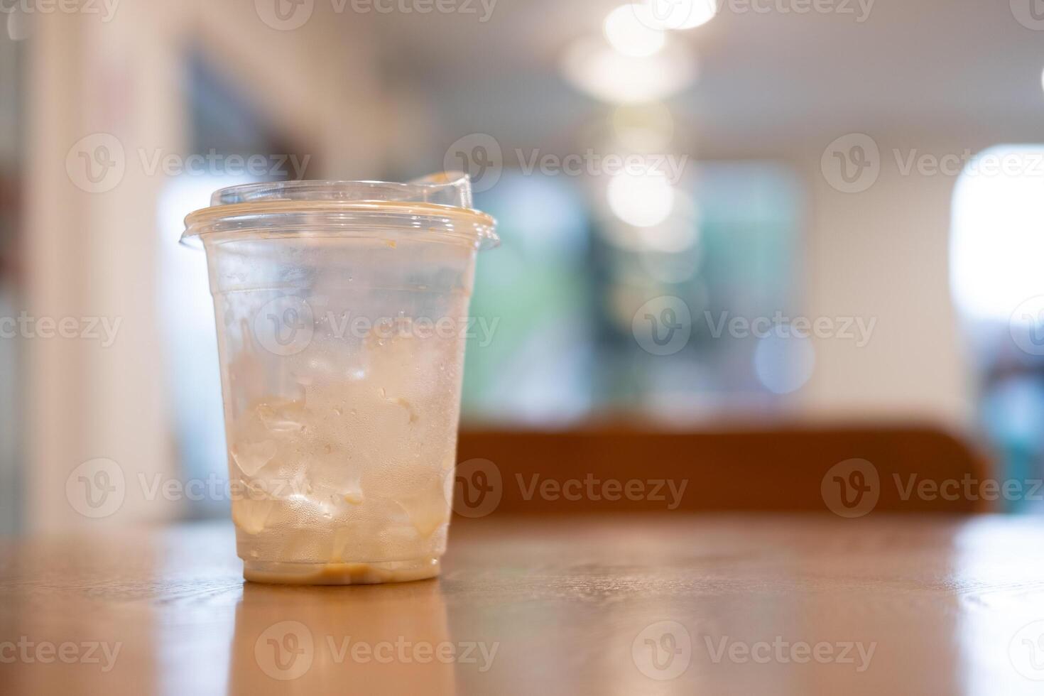 Iced coffee plastic cup with a little ice on wood desk blurred background photo