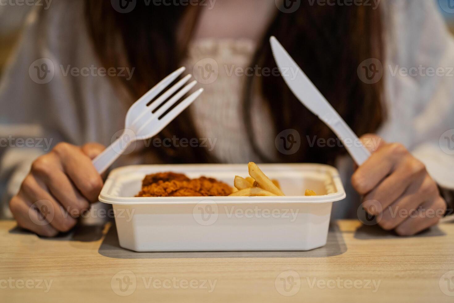 A woman is holding a tray of food with a fork and knife. The food consists of chicken and french fries. The woman is in a casual and relaxed mood, as she is enjoying her meal photo