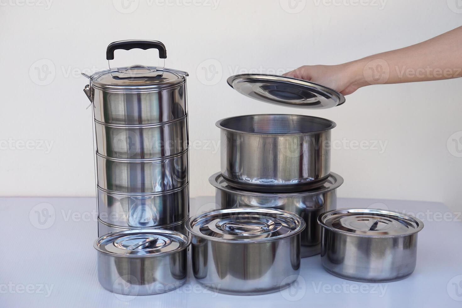 Hand open lid of set of stainless steel cookware and kitchen utensils. Pots, tray and tiffin box for containing food. Concept, safe container for food. photo