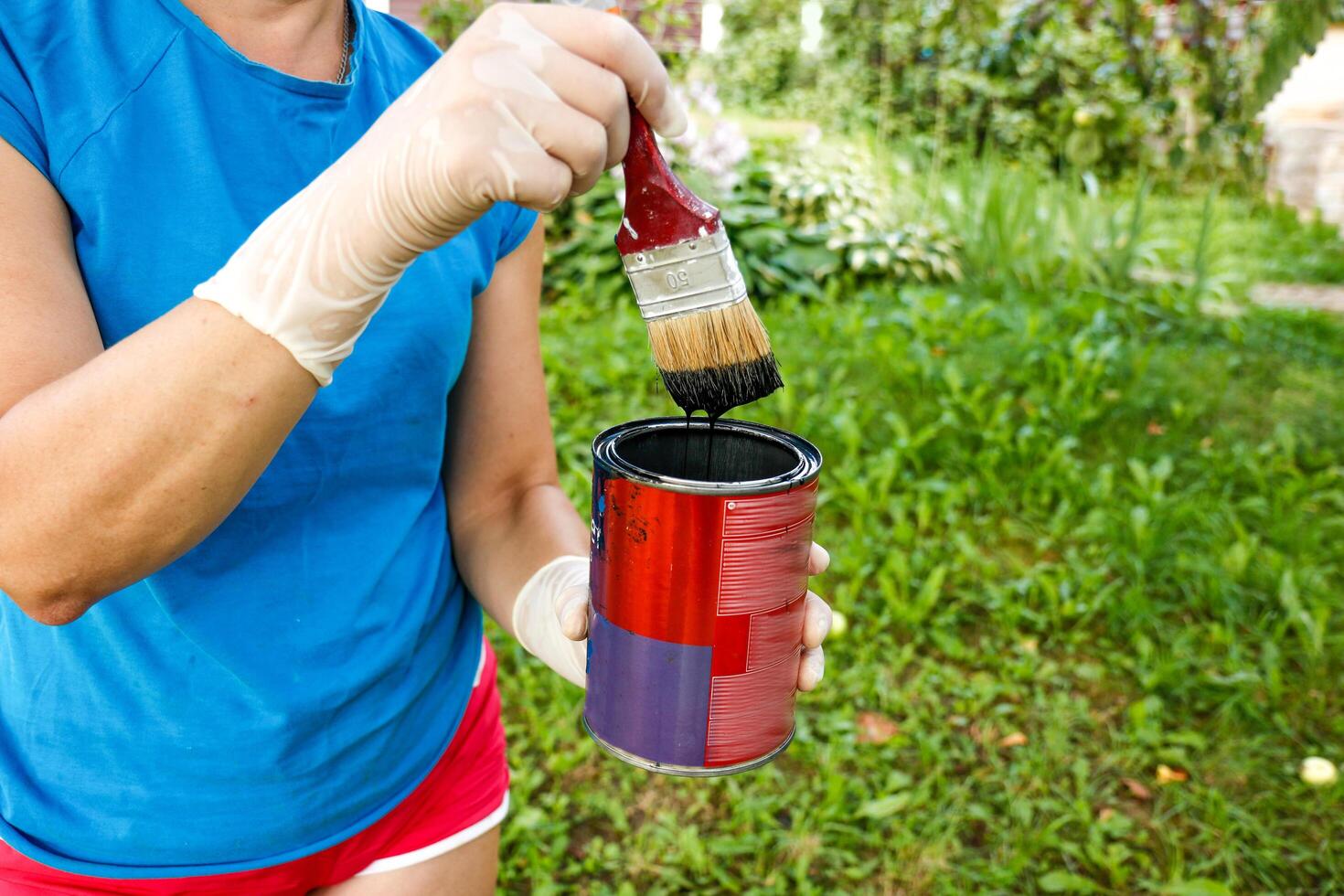 a woman's hand in a glove holds a brush with black paint flowing from it into a jar photo