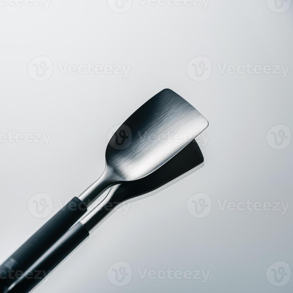 Close-up of a sleek stainless steel spatula with a black handle, reflecting on a smooth surface. photo