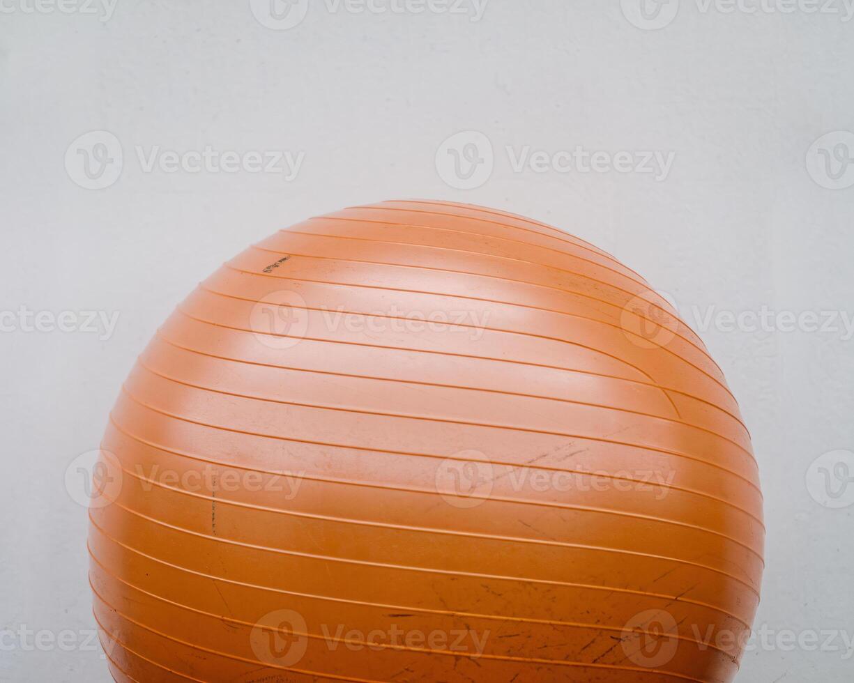 An orange exercise ball positioned against a minimalistic white wall. photo
