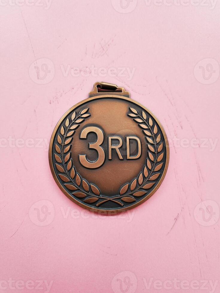 Bronze medal with '3RD' in the center, set against a soft pink background, symbolizing achievement. photo