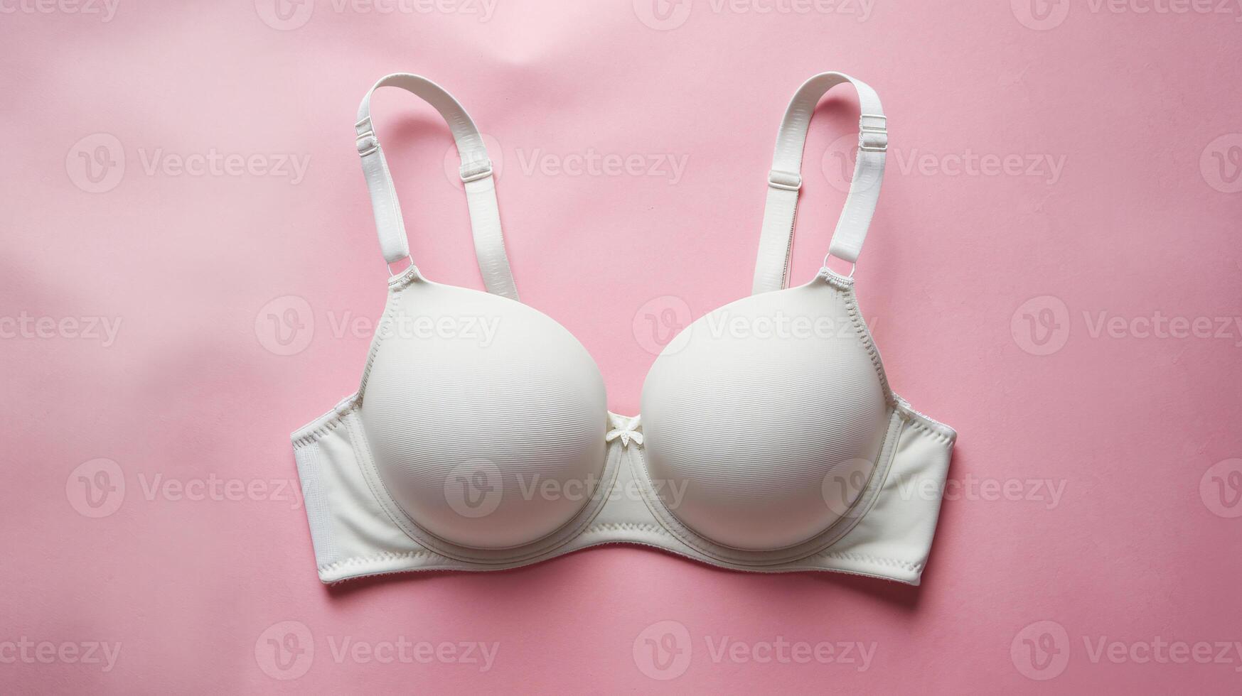Elegant white bra laid on a soft pink background, highlighting its smooth design and supportive structure. photo