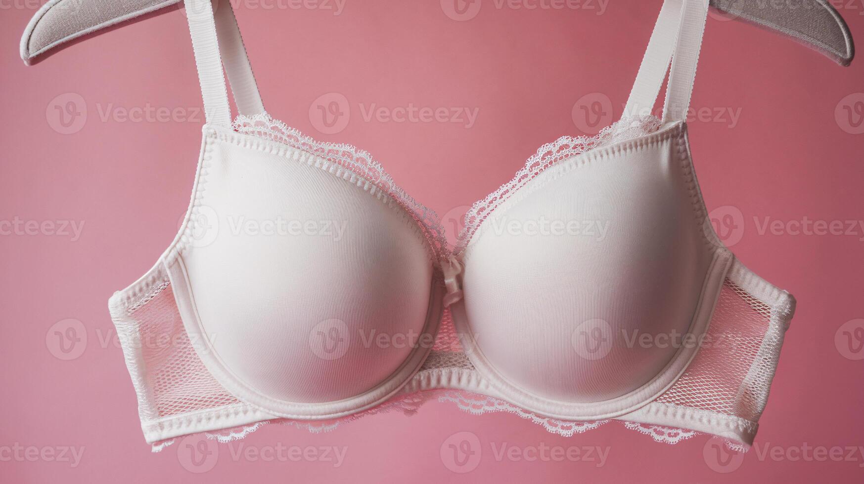 Elegant white lace bra suspended against a soft pink background, highlighting its delicate design. photo