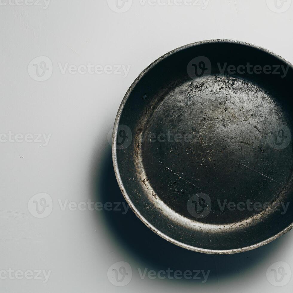 A vintage, well-used metal frying pan resting on a light surface, highlighting its rustic charm and history. photo