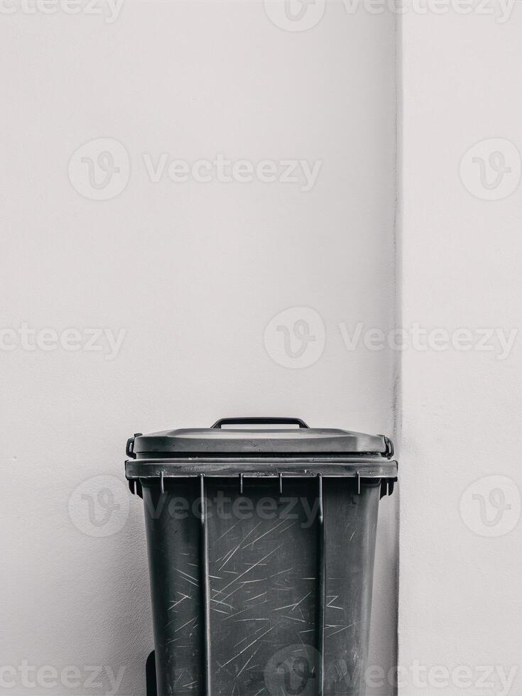 A black trash bin against a minimalist white wall, highlighting urban living and cleanliness. photo