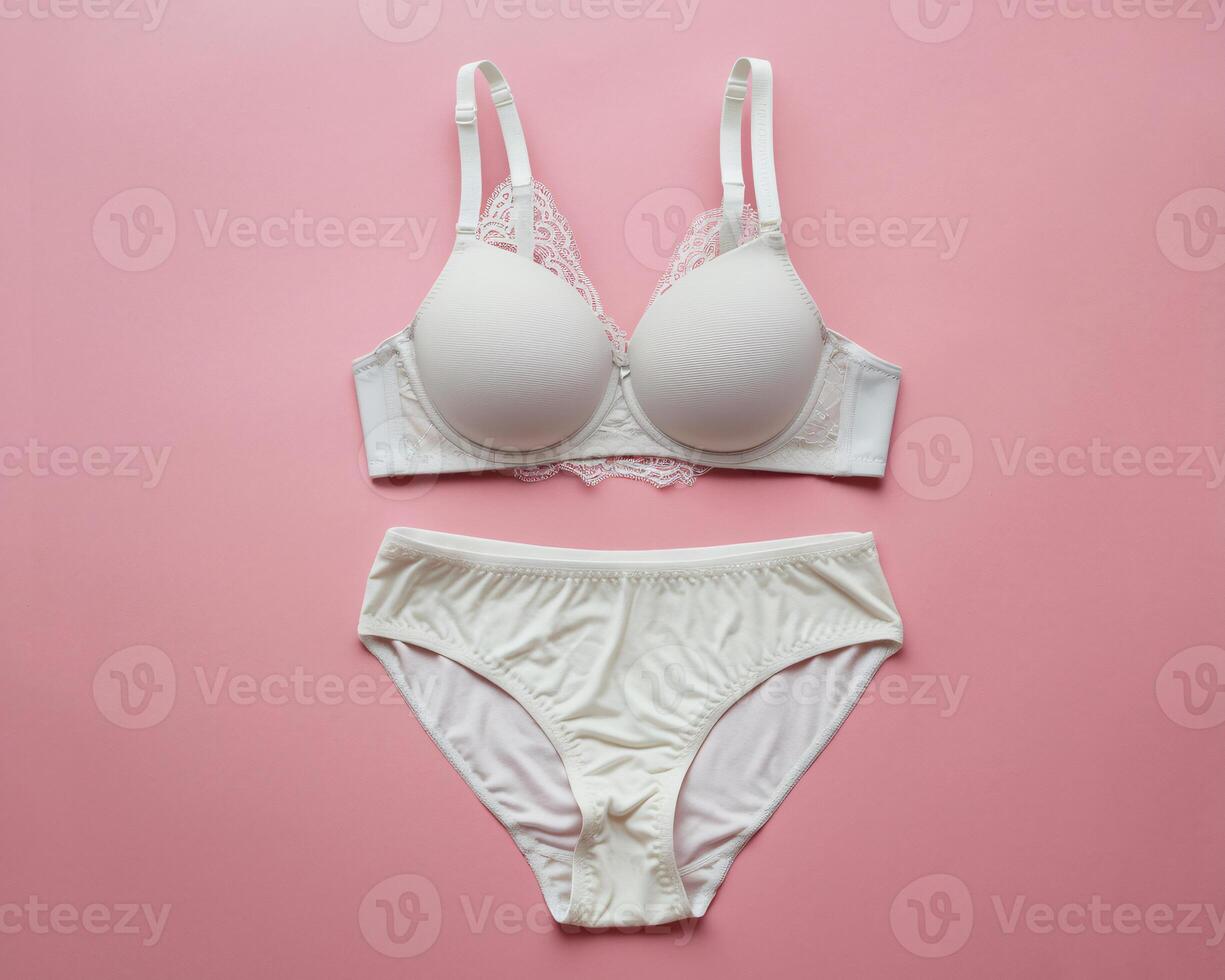 Elegant white lace bra and matching panties on a soft pink background. photo