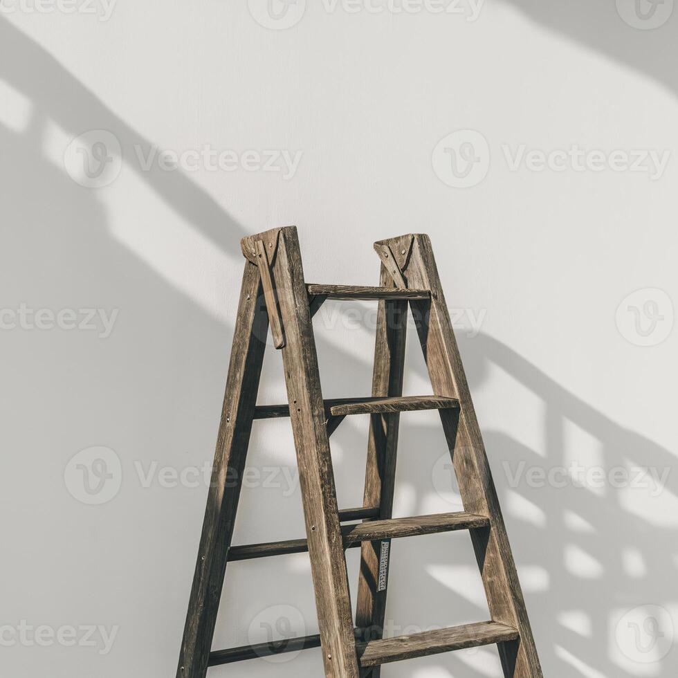 A rustic wooden ladder against a clean white wall, casting intriguing shadows. photo