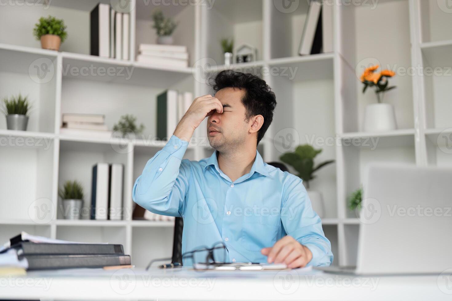 Stressed Office Worker Experiencing Headache from Overwork in Modern Workspace with Laptop and Documents photo