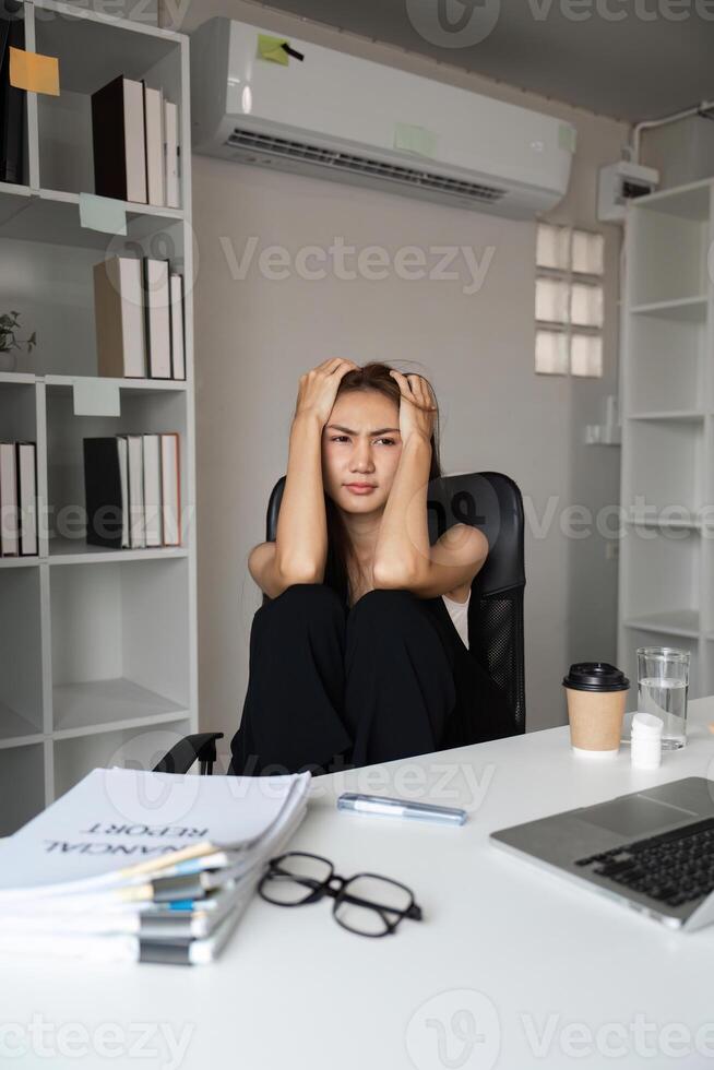 Stressed Office Worker Sitting at Desk with Documents and Laptop in Modern Workspace photo