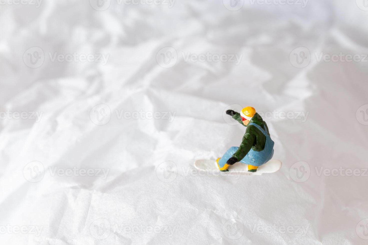 Miniature people snowboarder dressed in vibrant winter gear, carving through a snowy slope photo