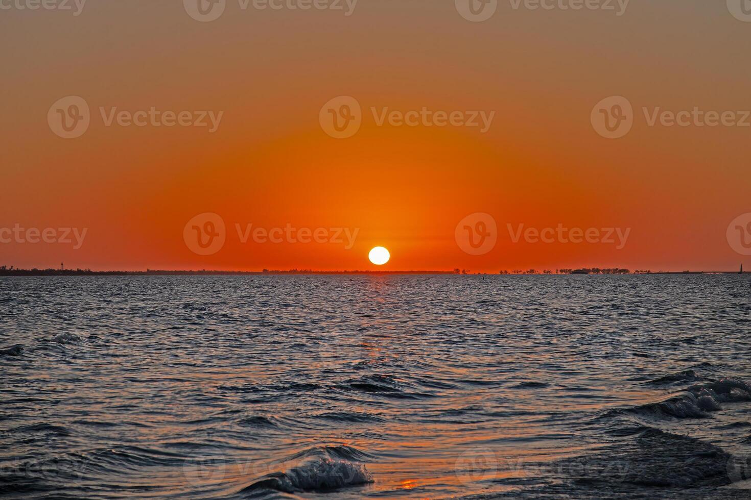 Breathtaking ocean sunset with vivid orange sky, gentle waves, and serene beach shoreline photo