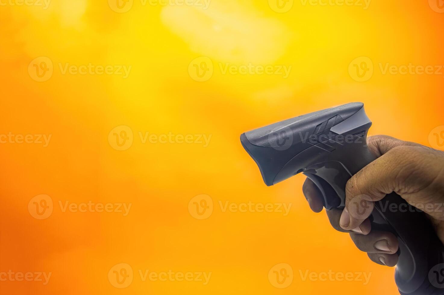 A hand holding a barcode scanner against a vibrant yellow orange background, highlighting the device ergonomic design and functionality. Ideal for retail and inventory management photo