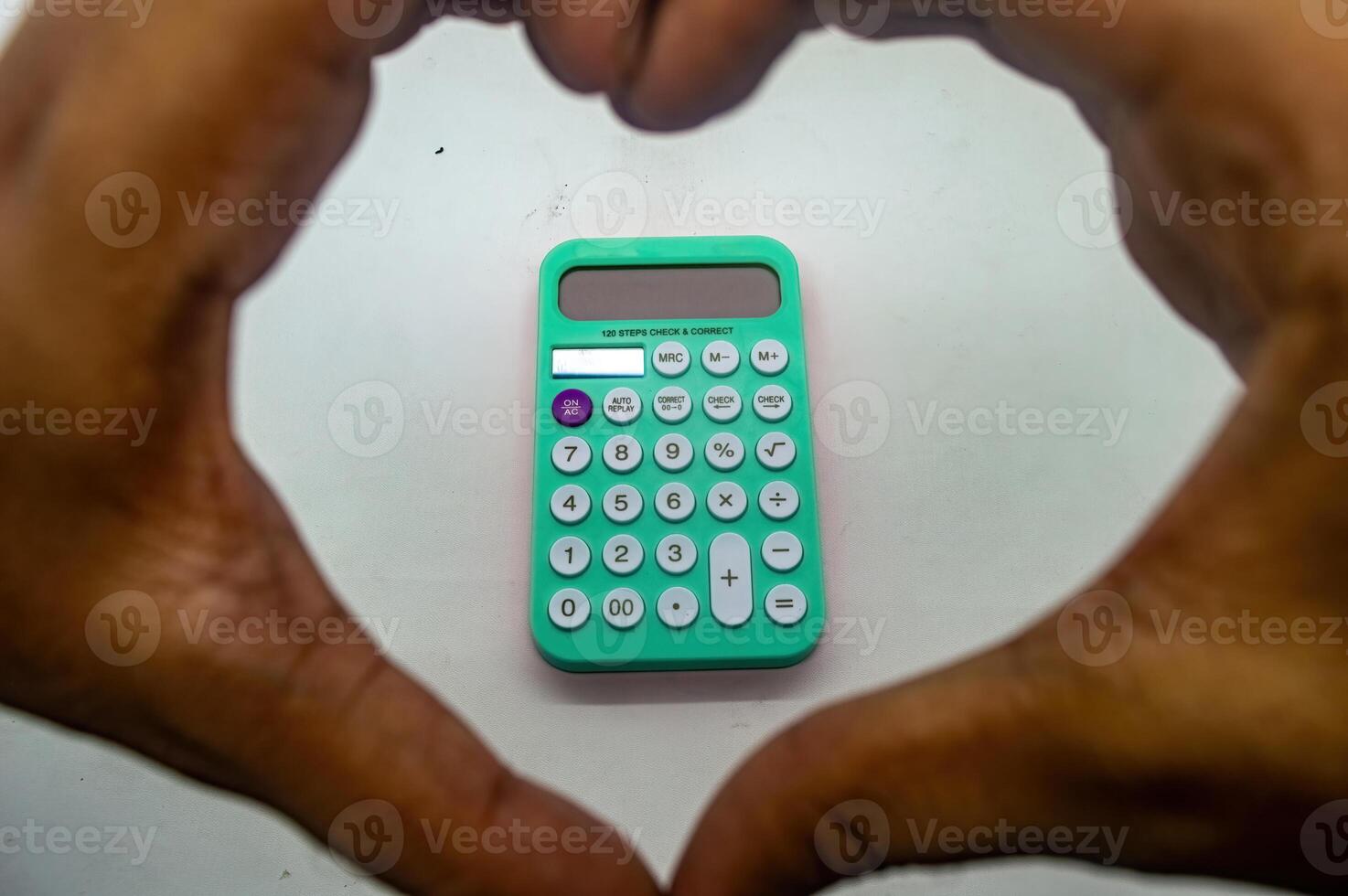 Hands forming a heart shape around a green calculator on a white background, symbolizing love for mathematics and calculations photo