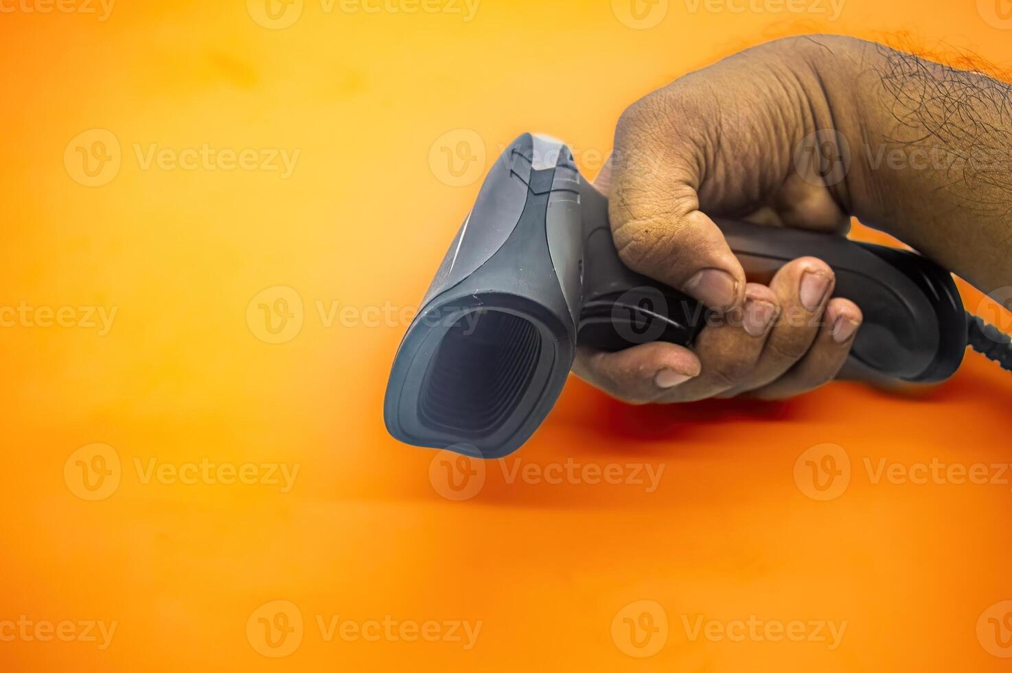 A hand holding a barcode scanner against an orange background, showcasing the device s ergonomic design and efficiency. Ideal for use in retail, inventory management, and point of sale applications photo