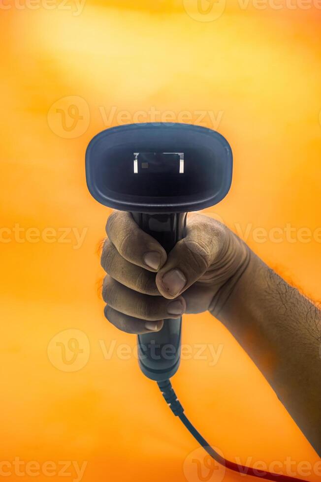 A hand holding a barcode scanner against an orange background, highlighting the device s ergonomic design and functionality. Ideal for retail, inventory, or point of sale applications photo