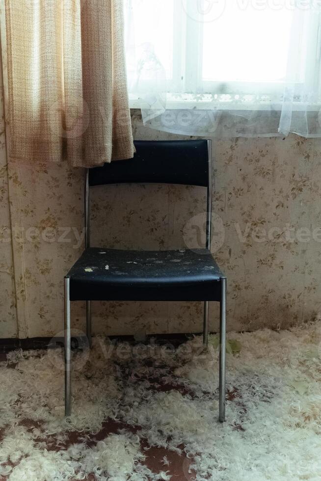 Forgotten chair in an abandoned room with scattered debris and sunlight filtering through a curtain photo