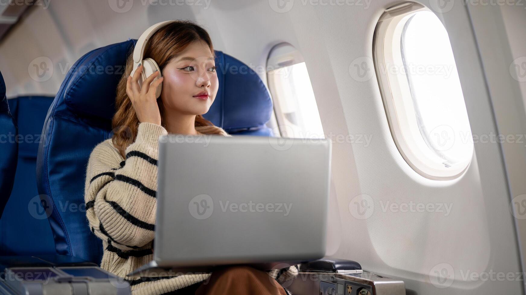 A beautiful woman gazes at the sky view and daydreams while working on her laptop during the flight. photo