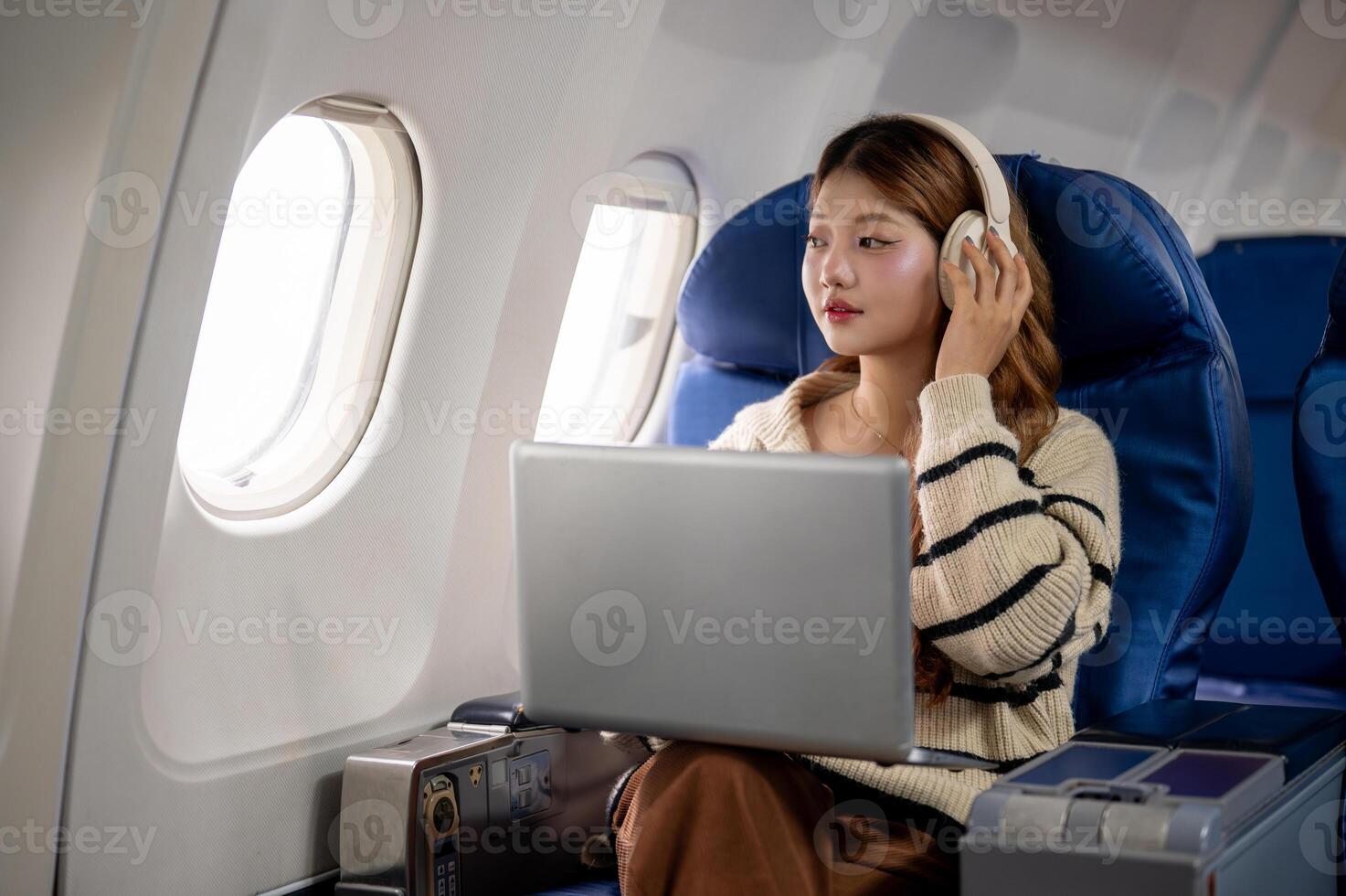 A beautiful woman gazes at the sky view and daydreams while working on her laptop during the flight. photo