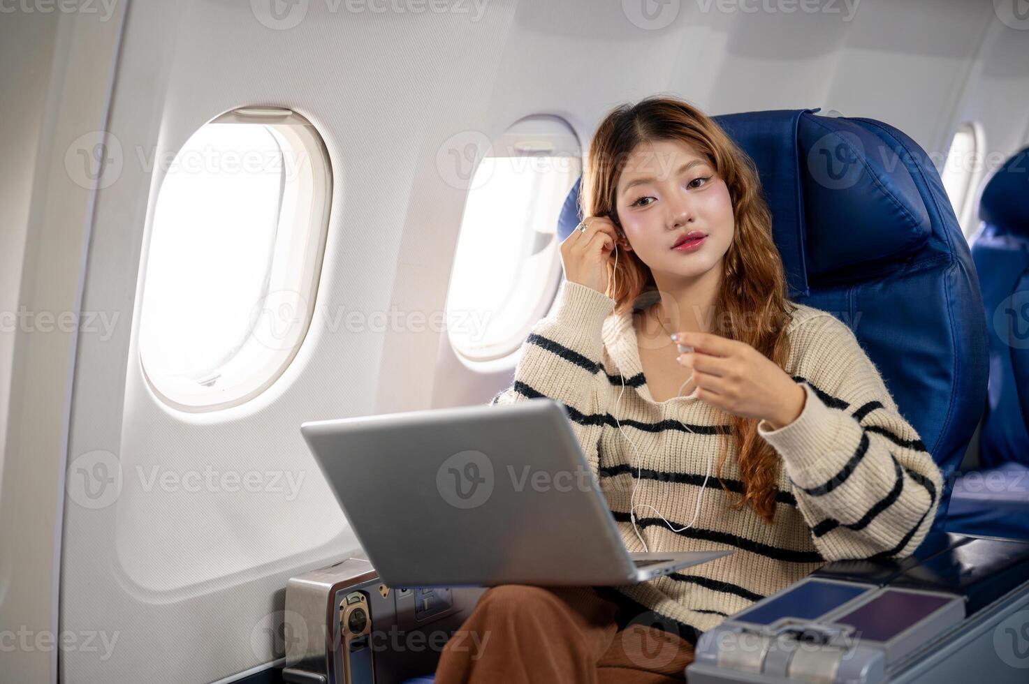 An attractive Asian woman wearing earphones and working on her laptop during the flight. photo