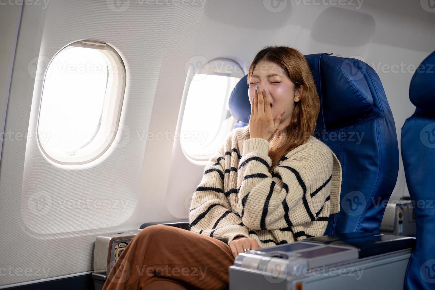 A tired, sleepy Asian woman yawning, feeling sleepy during the long flight to somewhere. photo