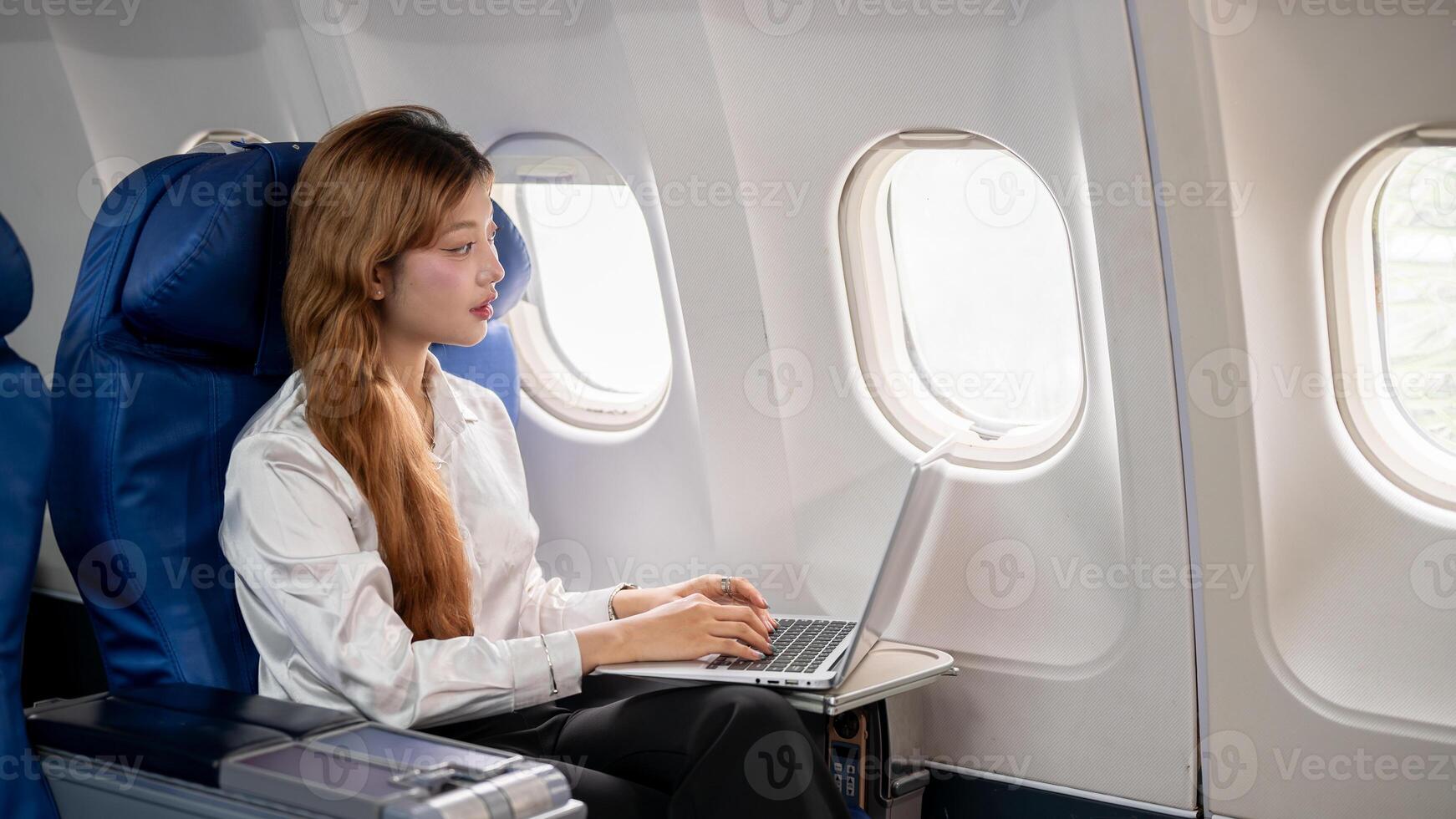 An Asian businesswoman gazes out the window while working on her laptop during the flight. photo