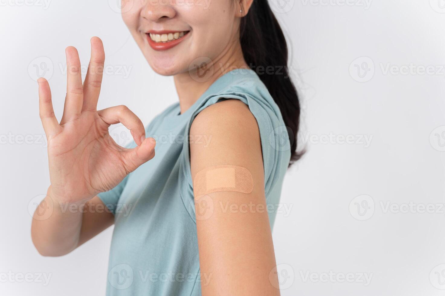 A carefree Asian woman showing her arm with a plaster adhesive bandage and giving a OK hand sign. photo