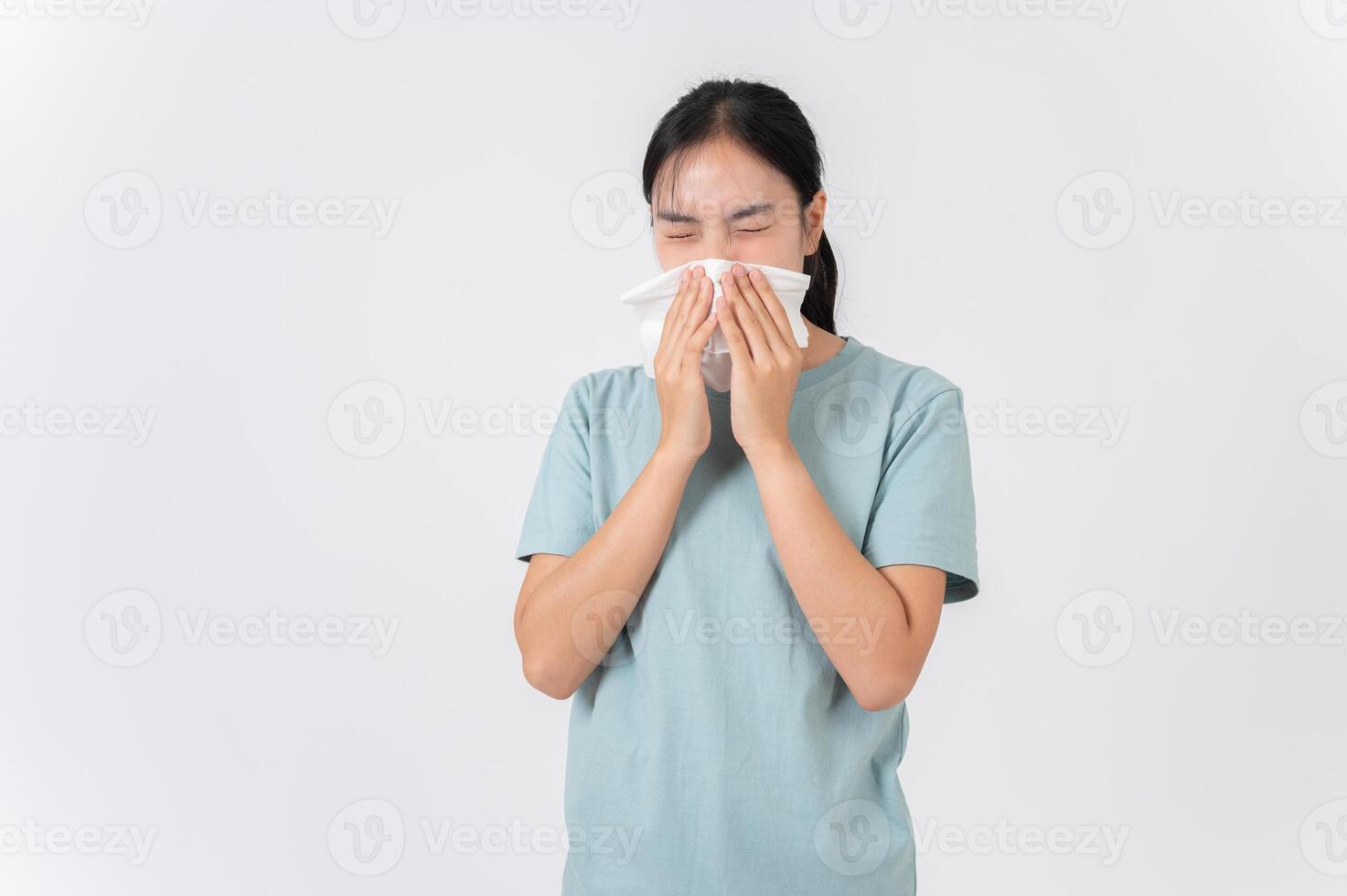 A sick Asian woman sneezing and blowing her nose, suffering from a runny nose, flu, or allergy. photo
