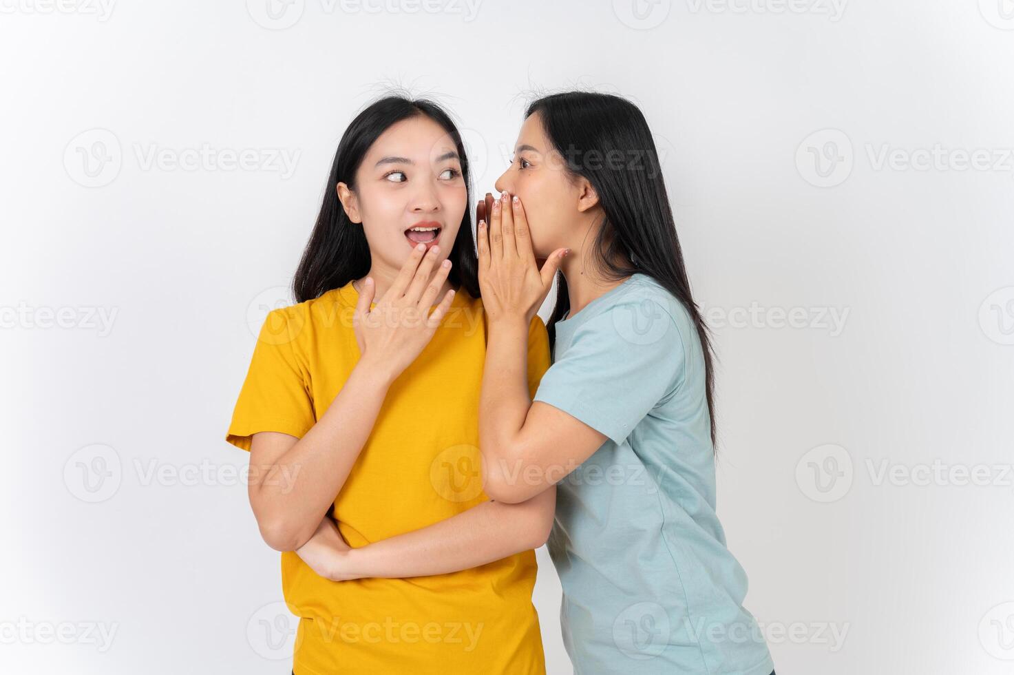 Two Asian female friends whispering a gossip secret to each other, with one amazed by the story. photo
