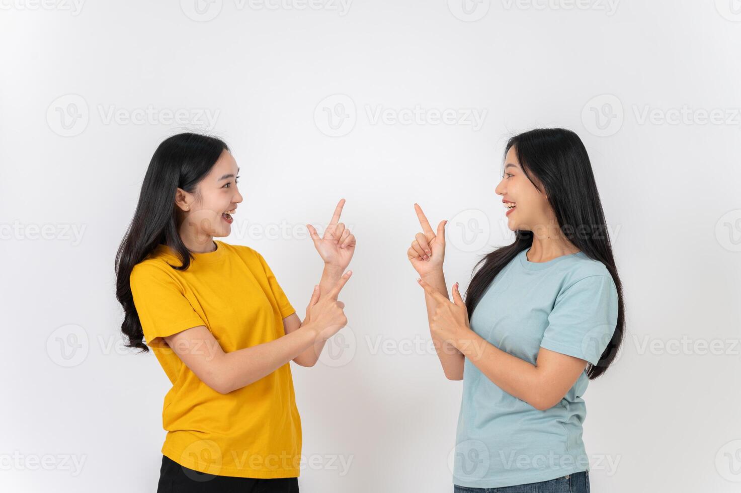 Two cheerful Asian female friends pointing their fingers upward as if recommending good news. photo