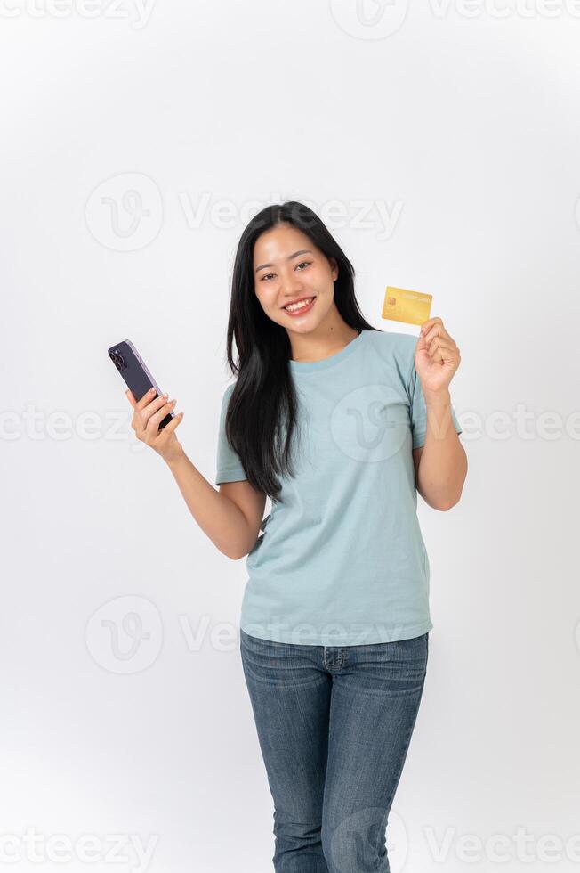 An Asian woman standing against a white studio background, holding a smartphone and a credit card. photo