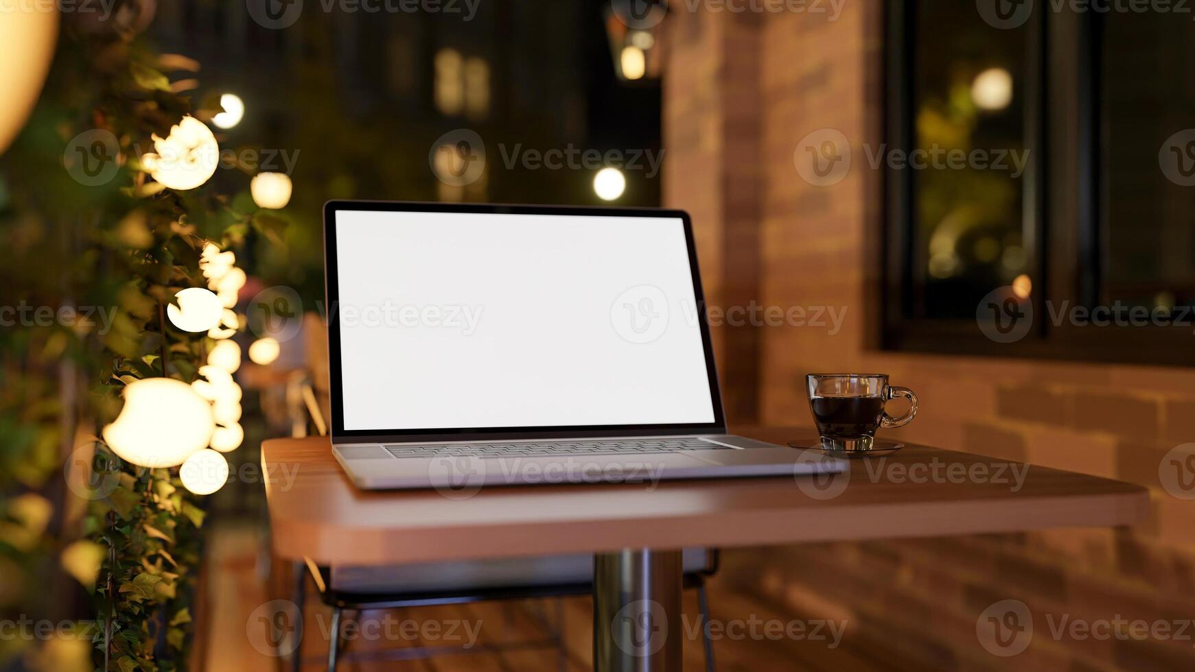 A close-up of a laptop on a table on an apartment balcony at night, illuminated by bulk lights. photo