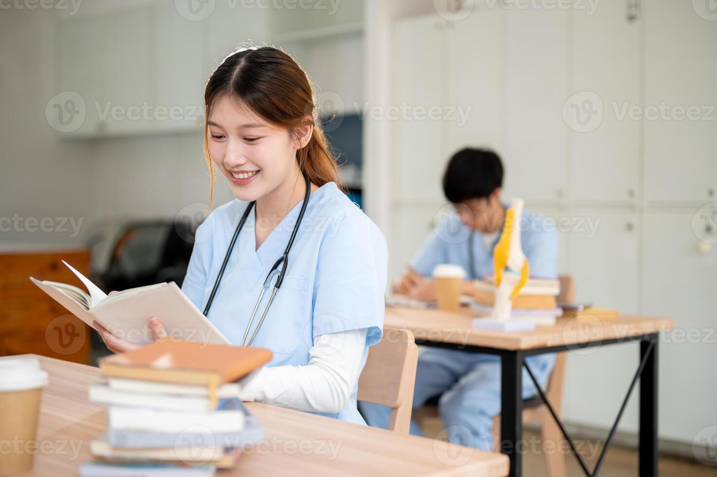 A smart and beautiful Asian female medical student in scrubs is reading or studying in the library. photo
