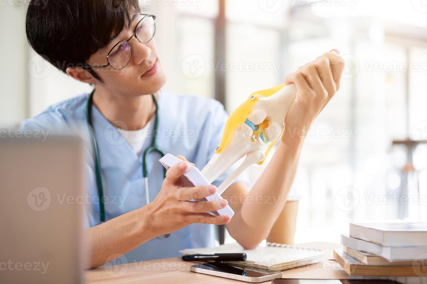 A smart Asian male medical student in scrubs is examining a model of bone joints. photo