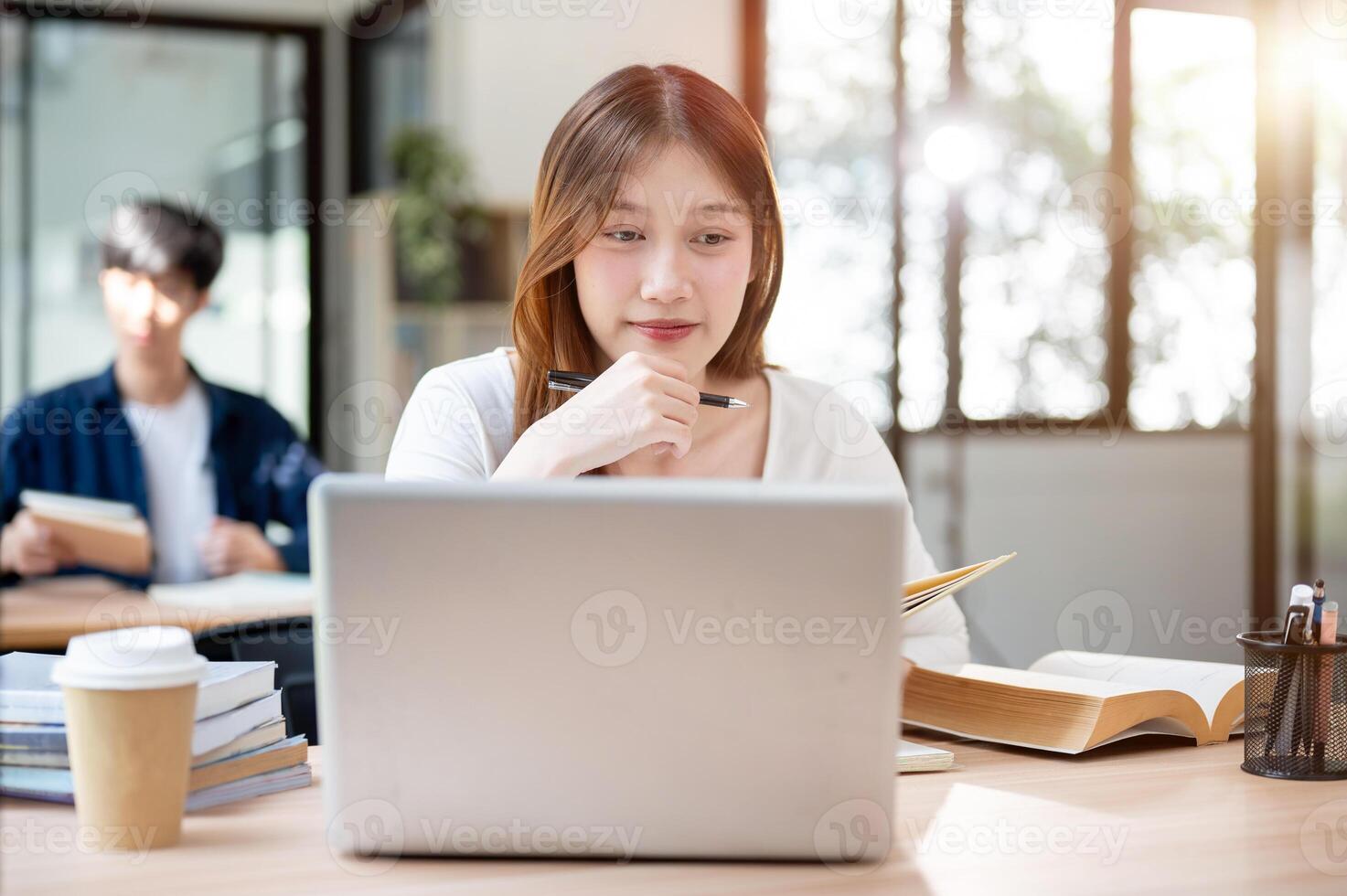 A smiling, happy Asian female college student working on her project on her laptop in a coffee shop. photo