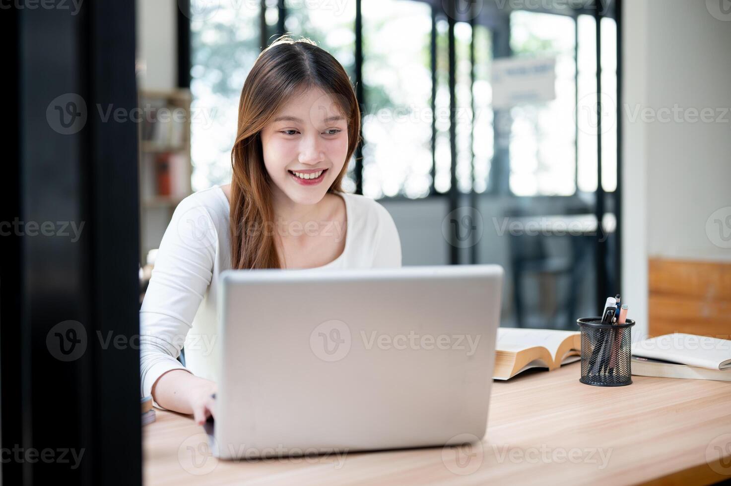 A smiling, happy Asian female college student working on her project on her laptop in a coffee shop. photo