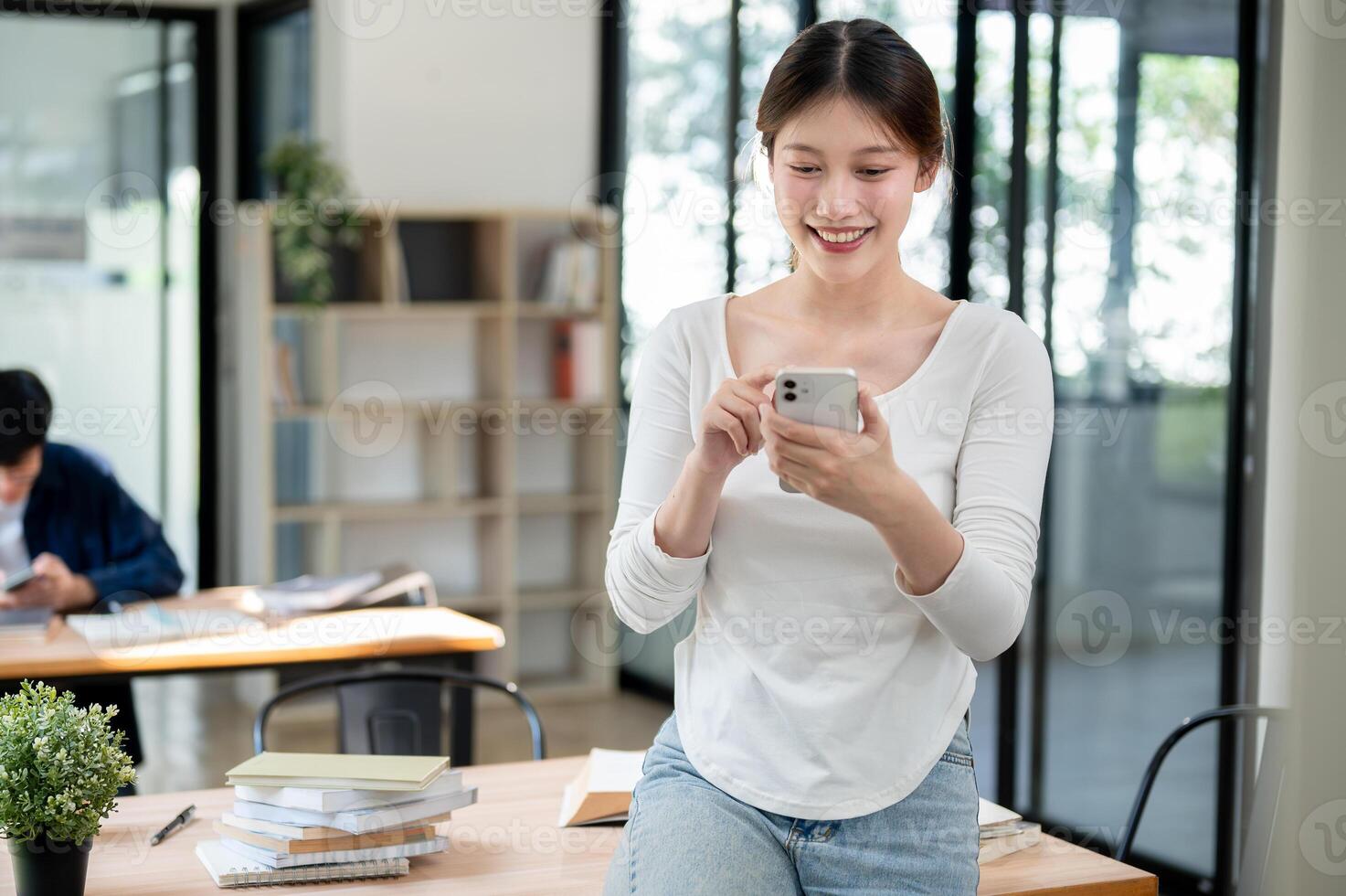 A smiling Asian female college student reading texts on her smartphone while standing in a library. photo
