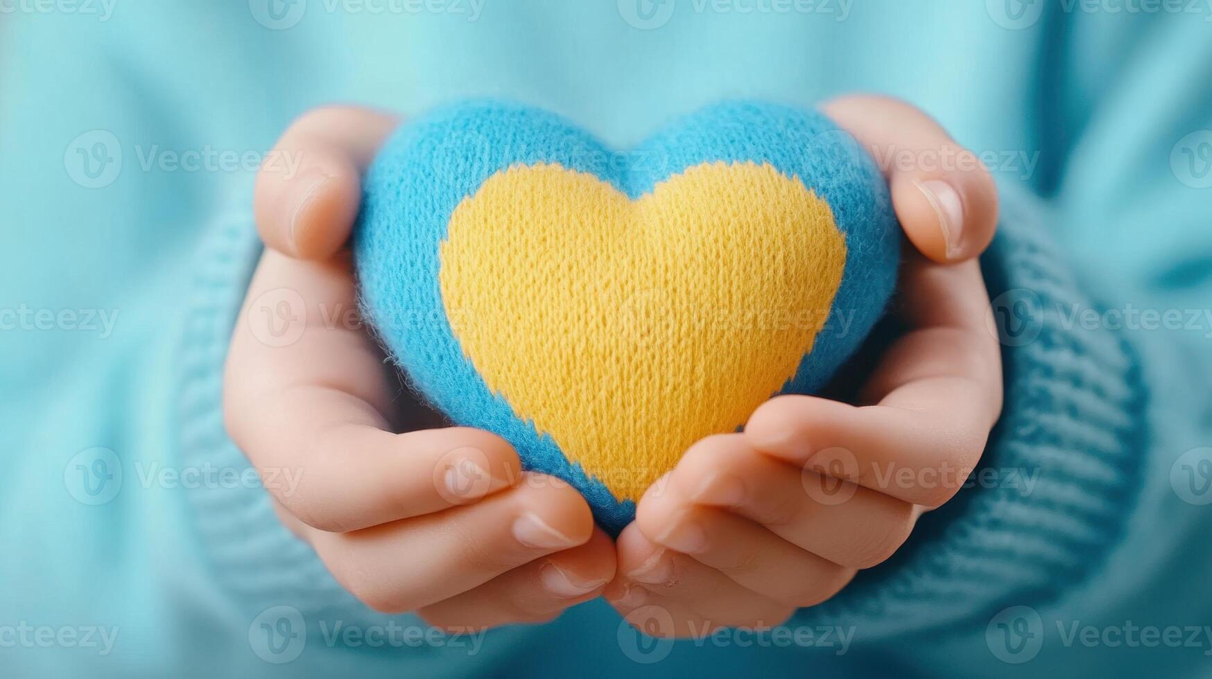 Child holding a heart with both hands, close-up. The heart is split in two colors, blue on the top half and yellow photo